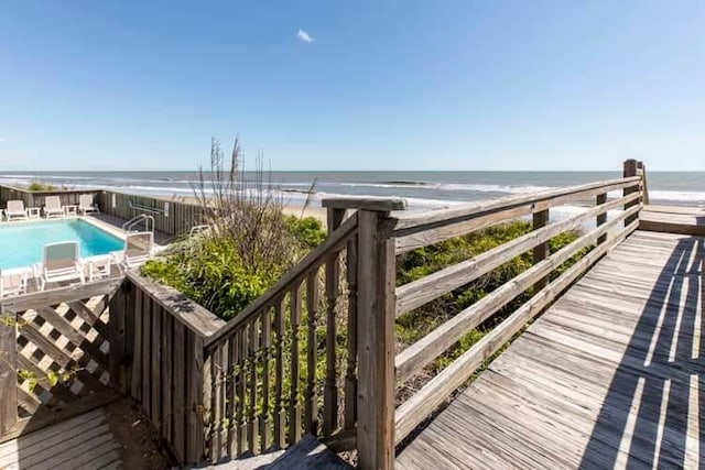 deck featuring a fenced in pool, a water view, and a view of the beach