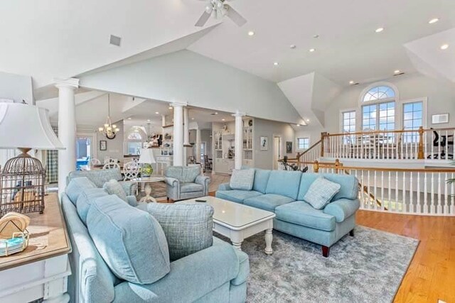 living area featuring lofted ceiling, ceiling fan with notable chandelier, wood finished floors, and ornate columns