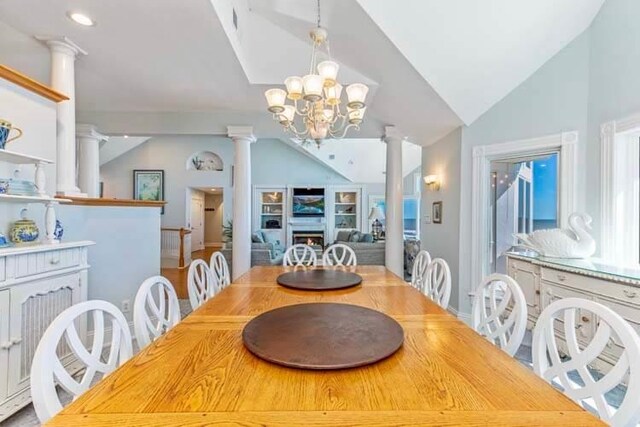 dining space featuring an inviting chandelier, lofted ceiling, a warm lit fireplace, and ornate columns