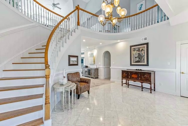 interior space featuring visible vents, a wainscoted wall, ceiling fan with notable chandelier, arched walkways, and a towering ceiling