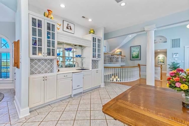 kitchen featuring visible vents, decorative columns, decorative backsplash, white dishwasher, and a sink