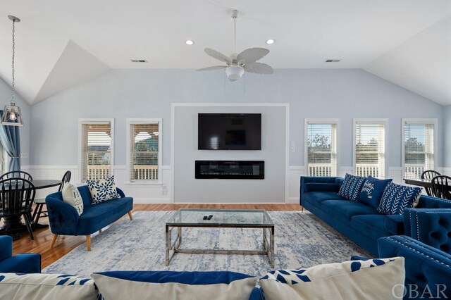 living area with lofted ceiling, a glass covered fireplace, visible vents, and a healthy amount of sunlight