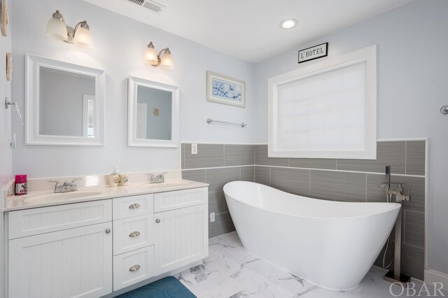 bathroom featuring double vanity, visible vents, a soaking tub, marble finish floor, and a sink