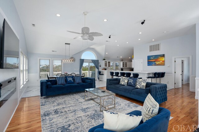 living area featuring light wood-type flooring, high vaulted ceiling, visible vents, and a wainscoted wall