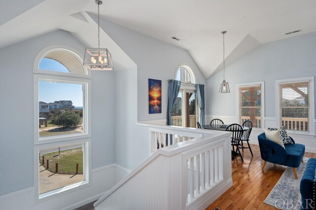 hall featuring lofted ceiling, a wainscoted wall, an upstairs landing, and wood finished floors