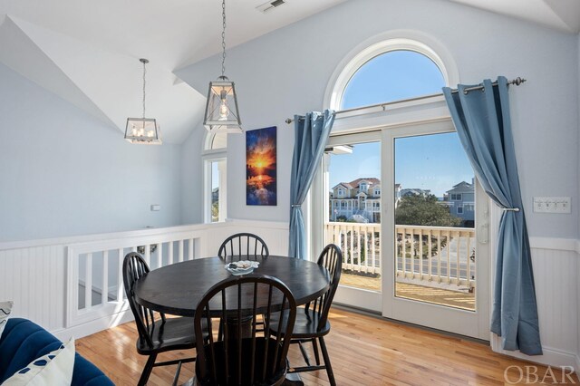 dining area with a wainscoted wall, vaulted ceiling, visible vents, and light wood finished floors