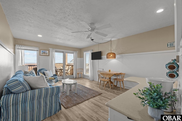 living room with light wood-type flooring, ceiling fan, a textured ceiling, and recessed lighting