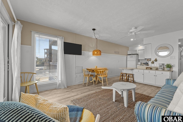 living area featuring light wood-style floors, ceiling fan, and a textured ceiling