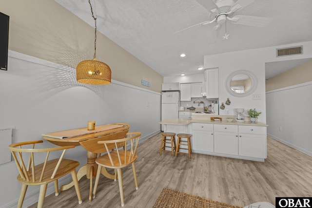 kitchen featuring decorative light fixtures, light countertops, visible vents, freestanding refrigerator, and white cabinets