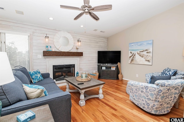 living room with a large fireplace, visible vents, lofted ceiling, ceiling fan, and wood finished floors