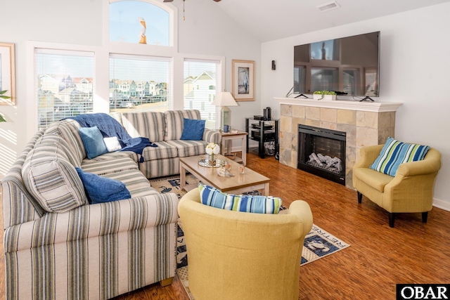 living room with visible vents, a ceiling fan, a tiled fireplace, wood finished floors, and high vaulted ceiling