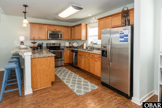 kitchen with light stone counters, a peninsula, appliances with stainless steel finishes, a kitchen bar, and pendant lighting