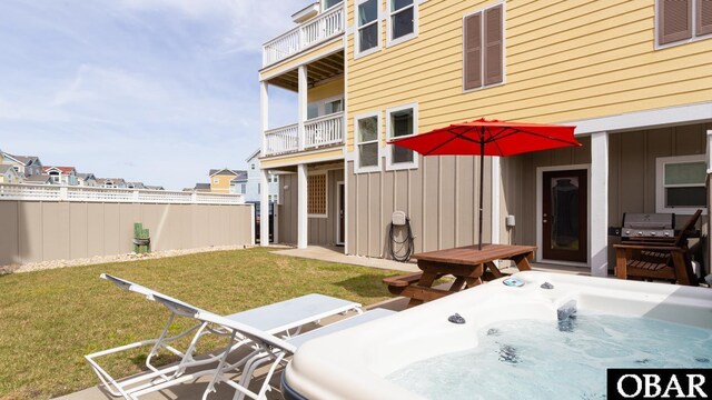 back of house with a balcony, a hot tub, board and batten siding, and a yard