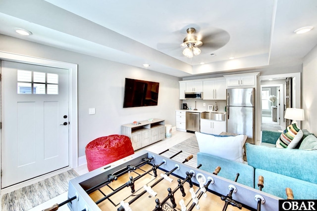 living area featuring baseboards, recessed lighting, a ceiling fan, and a tray ceiling