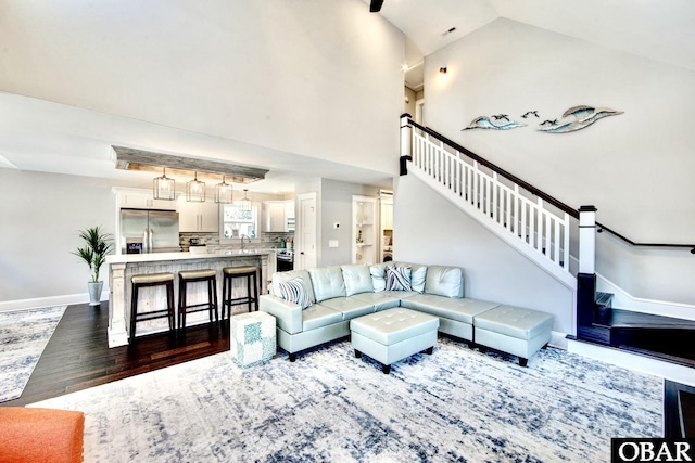 living area with dark wood-style floors, high vaulted ceiling, stairs, and baseboards