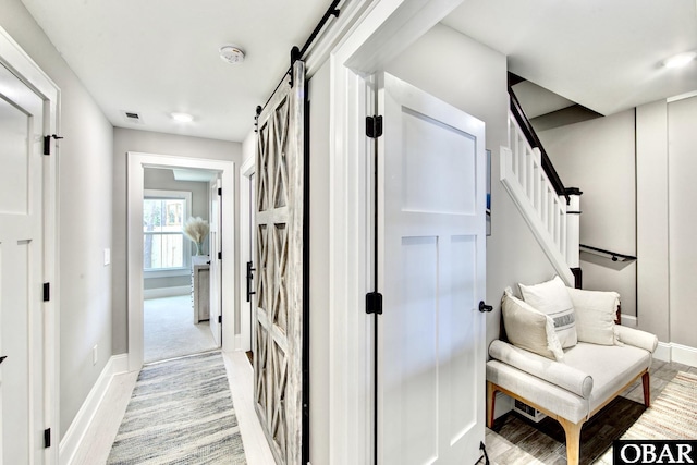 corridor featuring light wood-style flooring, baseboards, stairs, and a barn door