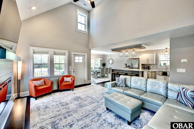 living area featuring a ceiling fan, wood finished floors, baseboards, and high vaulted ceiling