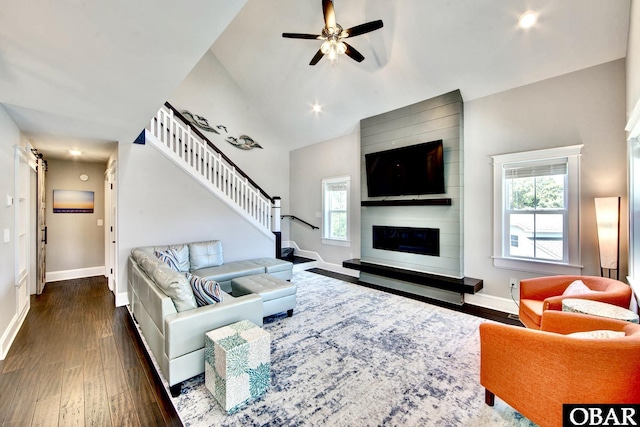 living area featuring a large fireplace, ceiling fan, baseboards, dark wood finished floors, and stairway