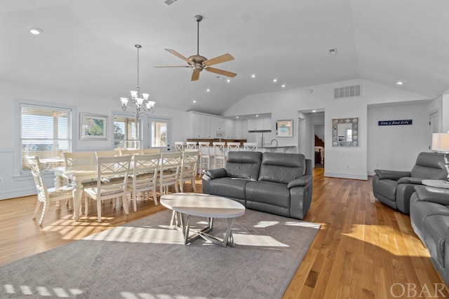 living area with visible vents, lofted ceiling, a wainscoted wall, light wood-style floors, and ceiling fan with notable chandelier