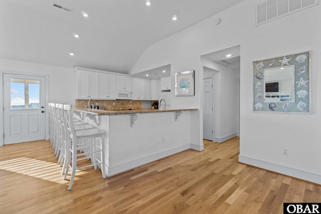 kitchen with stone counters, white cabinetry, visible vents, and white microwave