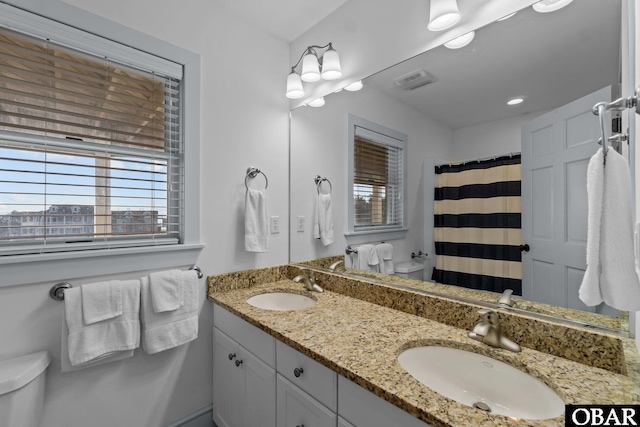 bathroom featuring double vanity, a shower with shower curtain, a sink, and toilet