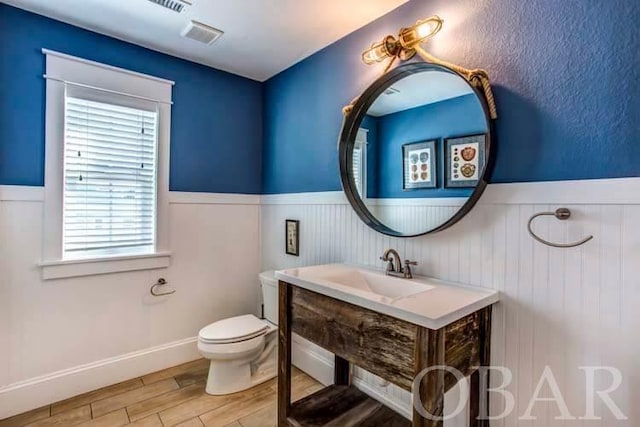 half bath featuring toilet, wood finished floors, a sink, and wainscoting