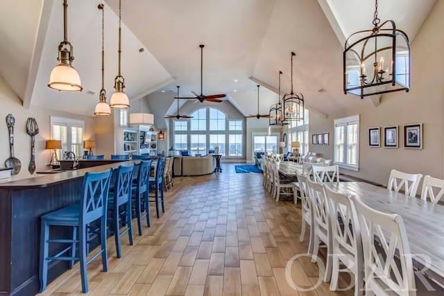 dining space with light wood-style flooring, high vaulted ceiling, and ceiling fan with notable chandelier