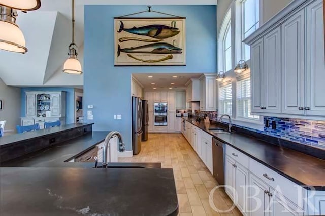 kitchen featuring dark countertops, a sink, white cabinets, and pendant lighting