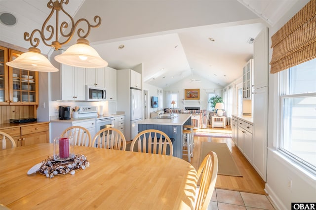 dining space with visible vents, a ceiling fan, a fireplace, light tile patterned floors, and vaulted ceiling