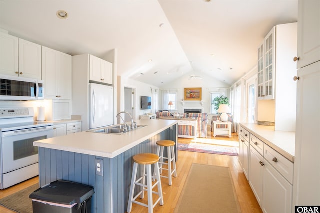 kitchen with lofted ceiling, a fireplace, white appliances, white cabinetry, and a sink