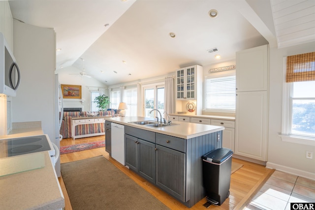 kitchen featuring a fireplace, a kitchen island with sink, gray cabinets, a sink, and vaulted ceiling