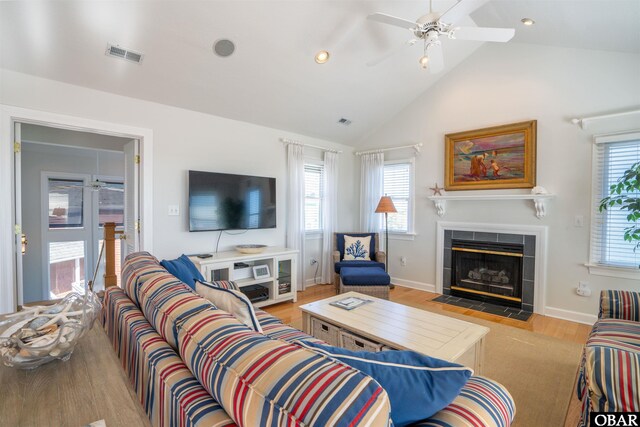 living room featuring a tiled fireplace, lofted ceiling, a healthy amount of sunlight, and visible vents