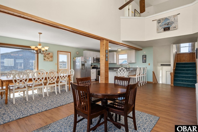dining area featuring light wood-type flooring, a high ceiling, baseboards, a chandelier, and stairs