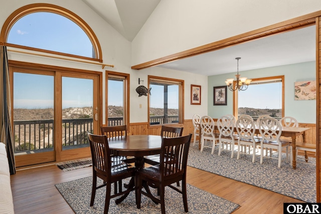 dining area featuring a wainscoted wall, wood walls, vaulted ceiling, an inviting chandelier, and wood finished floors