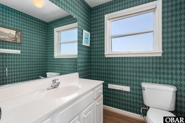 bathroom with wallpapered walls, toilet, vanity, and baseboards