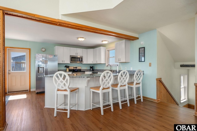 kitchen featuring a kitchen bar, wood finished floors, stainless steel appliances, a peninsula, and white cabinets