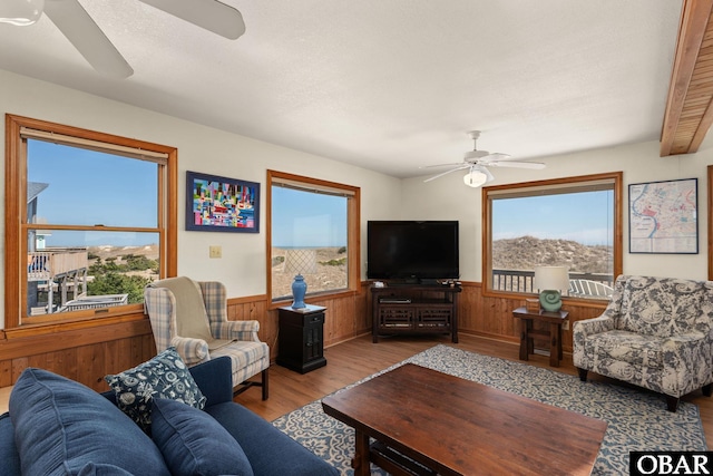 living room featuring a wealth of natural light, a wainscoted wall, and a ceiling fan