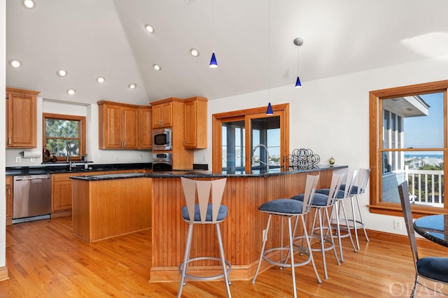 kitchen with light wood-style flooring, pendant lighting, stainless steel appliances, and dark stone countertops