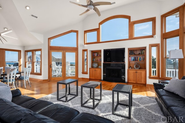 living room featuring a fireplace with raised hearth, high vaulted ceiling, light wood-style flooring, and baseboards