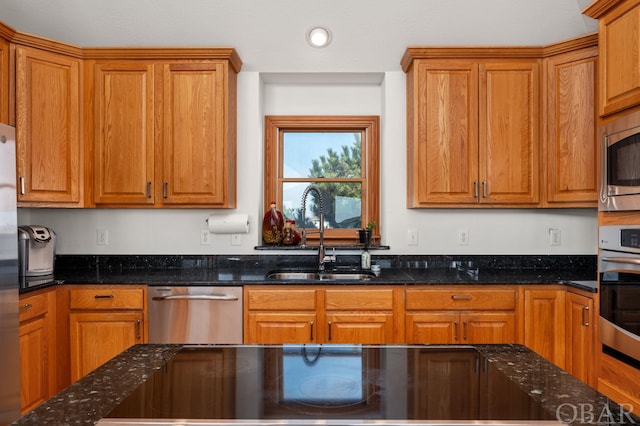 kitchen with appliances with stainless steel finishes, a sink, and dark stone countertops