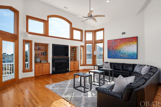 living room featuring light wood-style floors, a fireplace with raised hearth, visible vents, and built in shelves