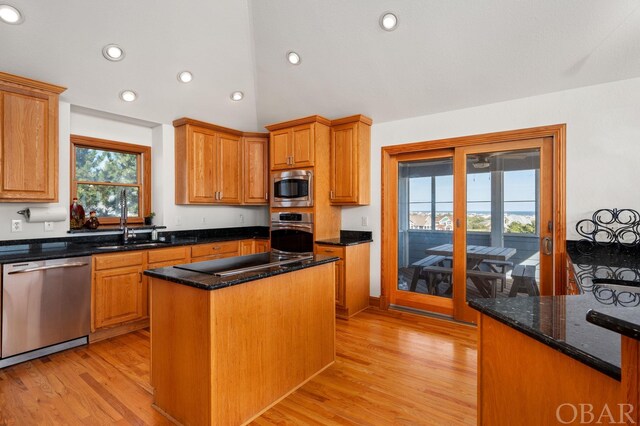 kitchen featuring lofted ceiling, light wood-style flooring, dark stone countertops, a center island, and stainless steel appliances