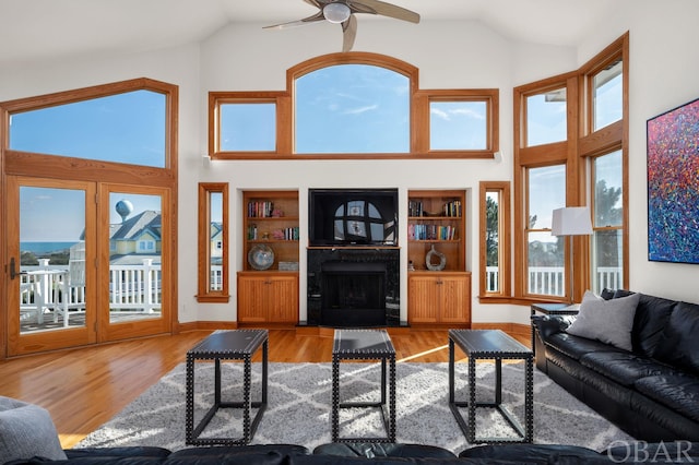 living area with a fireplace with flush hearth, high vaulted ceiling, light wood-style flooring, and baseboards