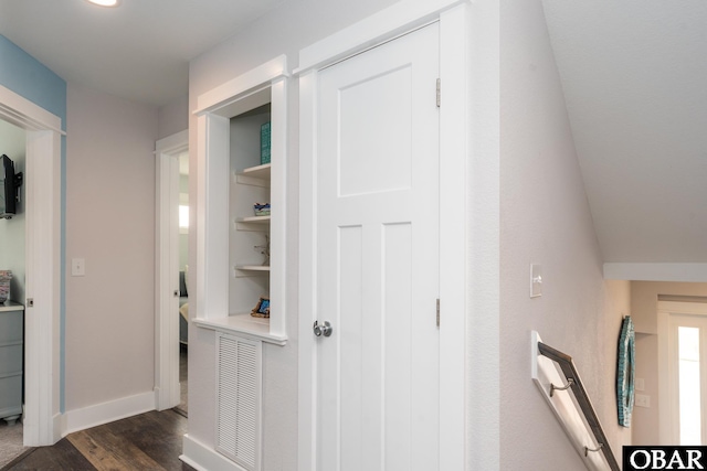 corridor featuring dark wood-type flooring, built in features, visible vents, and baseboards