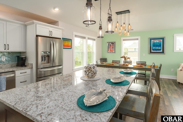 kitchen featuring a kitchen breakfast bar, dark wood finished floors, white cabinetry, appliances with stainless steel finishes, and light stone countertops