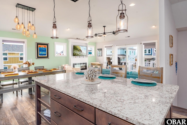 kitchen with dark brown cabinetry, decorative light fixtures, a fireplace, wood finished floors, and a ceiling fan