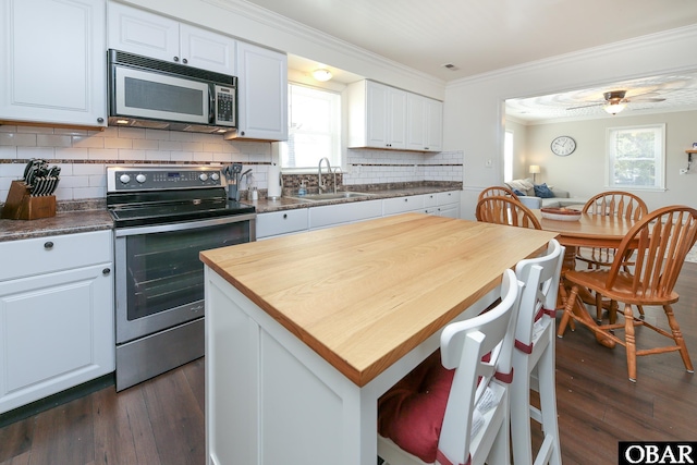 kitchen featuring dark wood-style floors, crown molding, appliances with stainless steel finishes, white cabinetry, and a sink