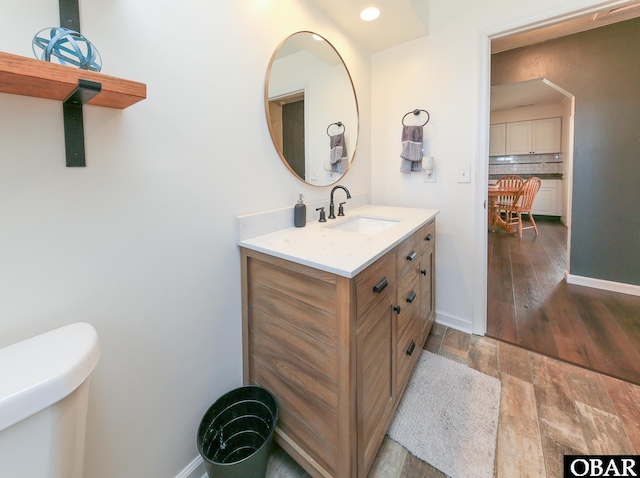 half bath featuring backsplash, toilet, vanity, wood finished floors, and baseboards