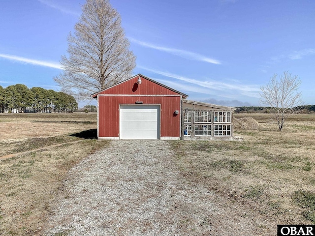 view of outbuilding with a garage, driveway, a rural view, and an outbuilding