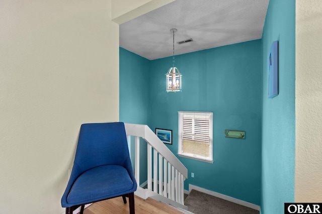 living area with a chandelier, visible vents, wood finished floors, baseboards, and an upstairs landing
